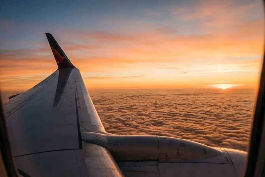Airplane wing above the clouds at sunset